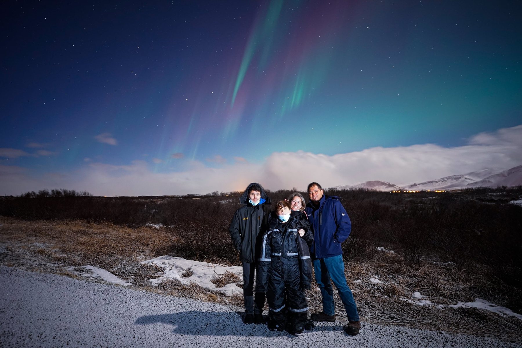 A family in thermal overalls posing on a gravel road under a faint aurora