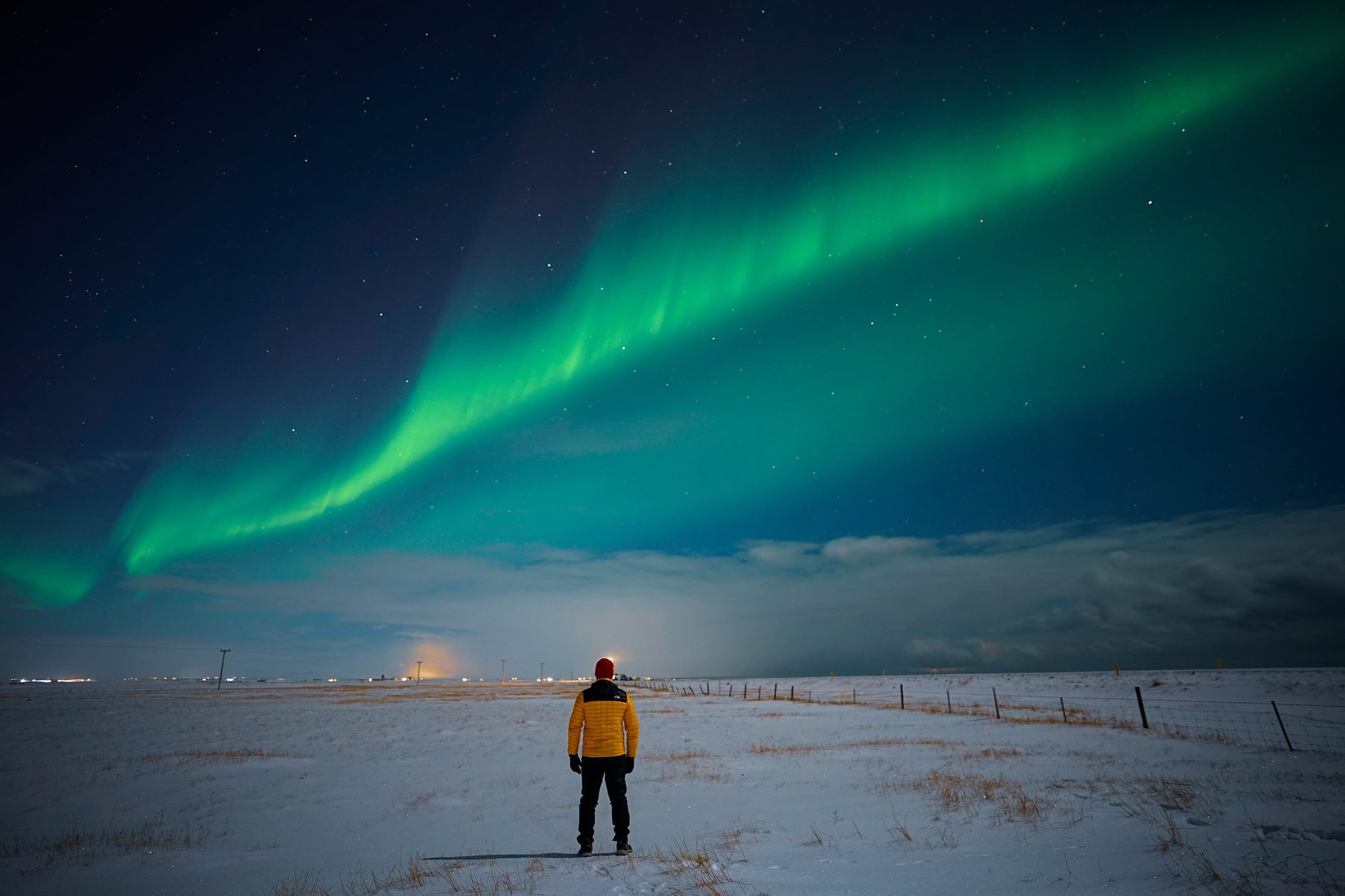 A guest in a yellow jacket standing alone under a broad aurora band