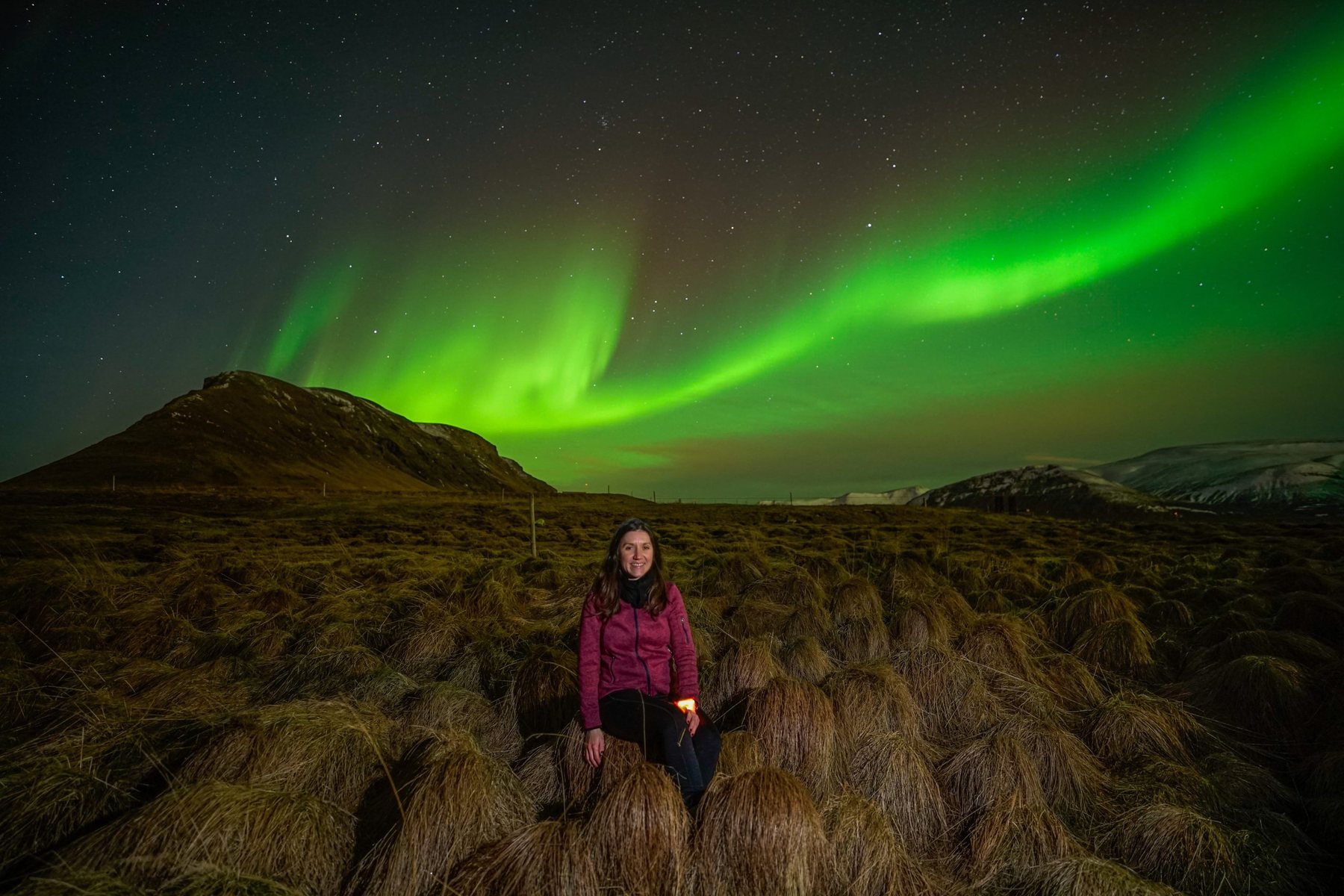 A guest seated on a mossy hillside as aurora streams across the sky
