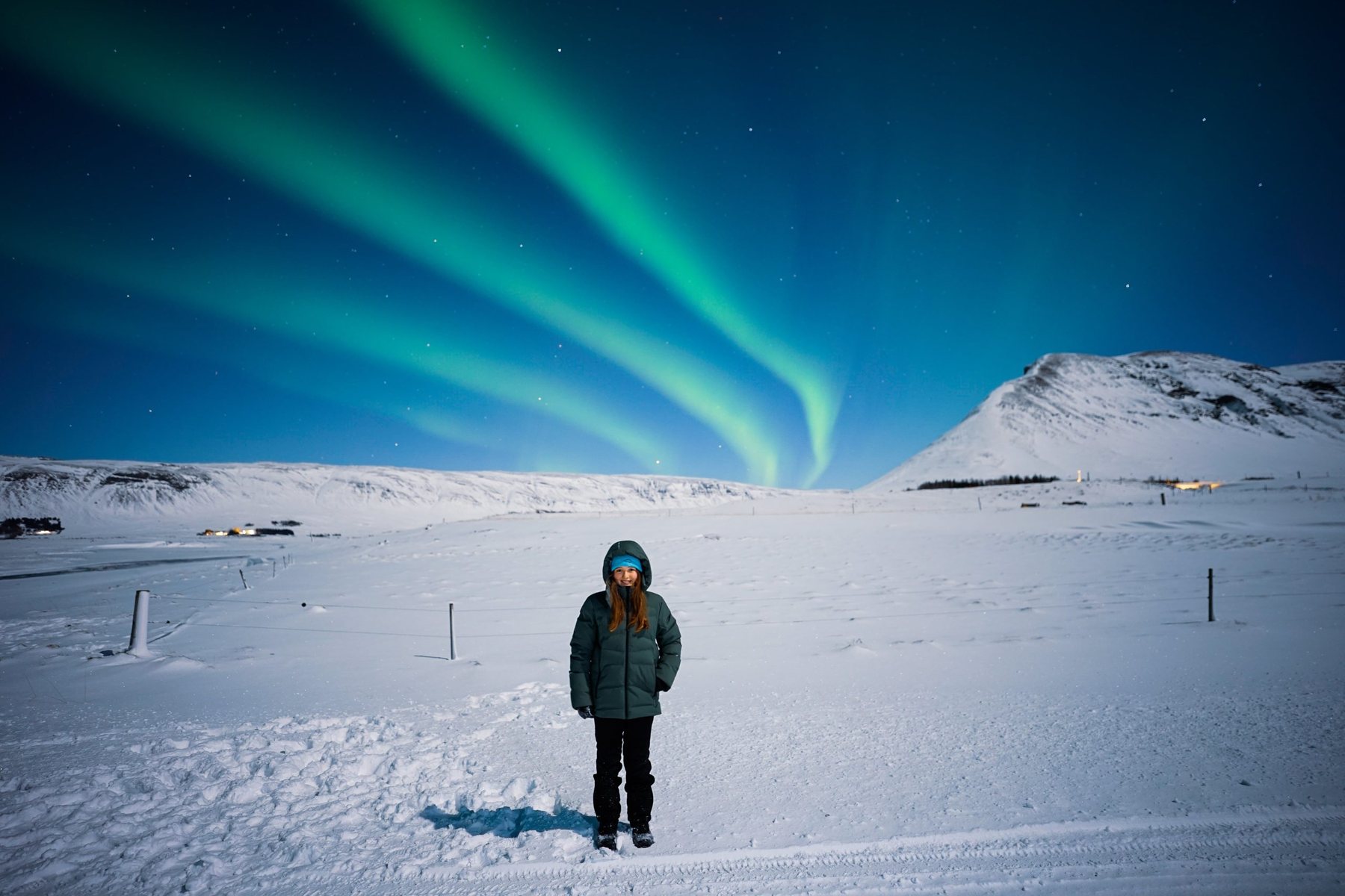 A guest alone on a moonlit snow plain beneath green aurora bands